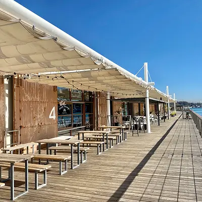 青空が広がる海沿いの、レトロな倉庫街のスライド写真。庇の下にテーブルとベンチが並んでいます